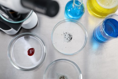 Photo of Petri dishes with samples and other glassware on metal table, flat lay