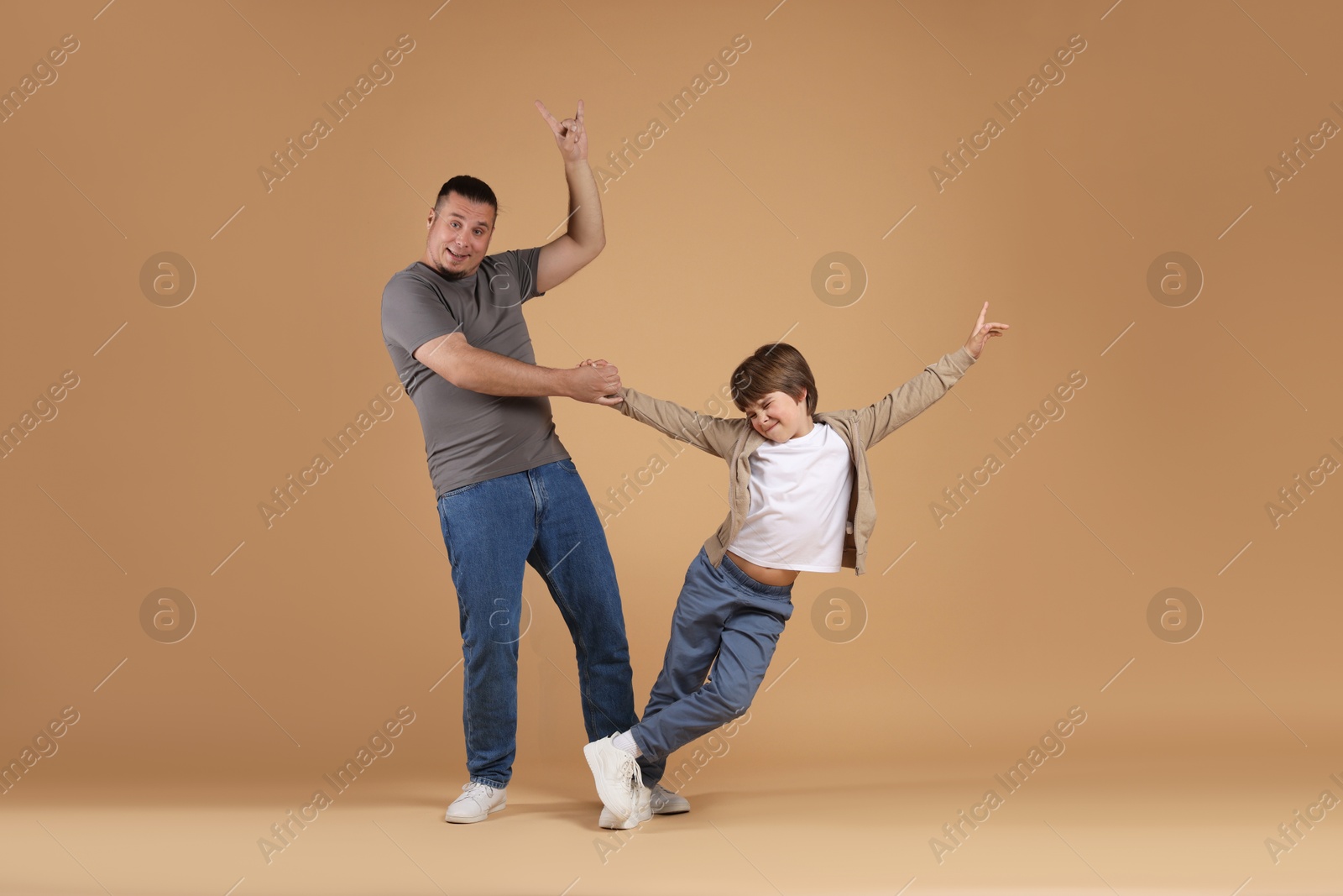 Father and his son dancing together on beige background Photo of Father and his son dancing together on beige background