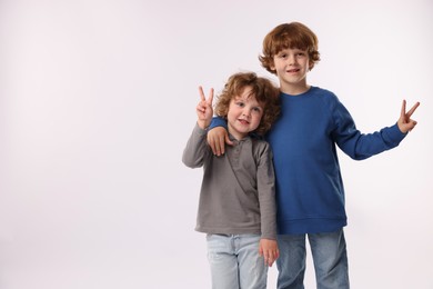 Photo of Cute little brothers showing V-signs on white background. Space for text
