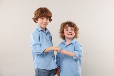 Photo of Cute little brothers bumping fists on light background
