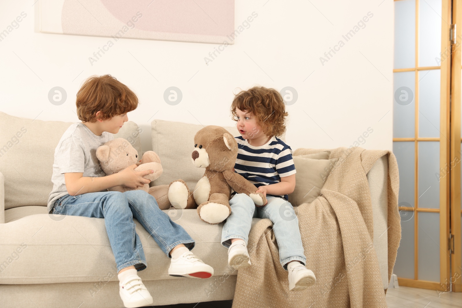 Cute little brothers playing with toys on sofa at home Photo of Cute little brothers playing with toys on sofa at home