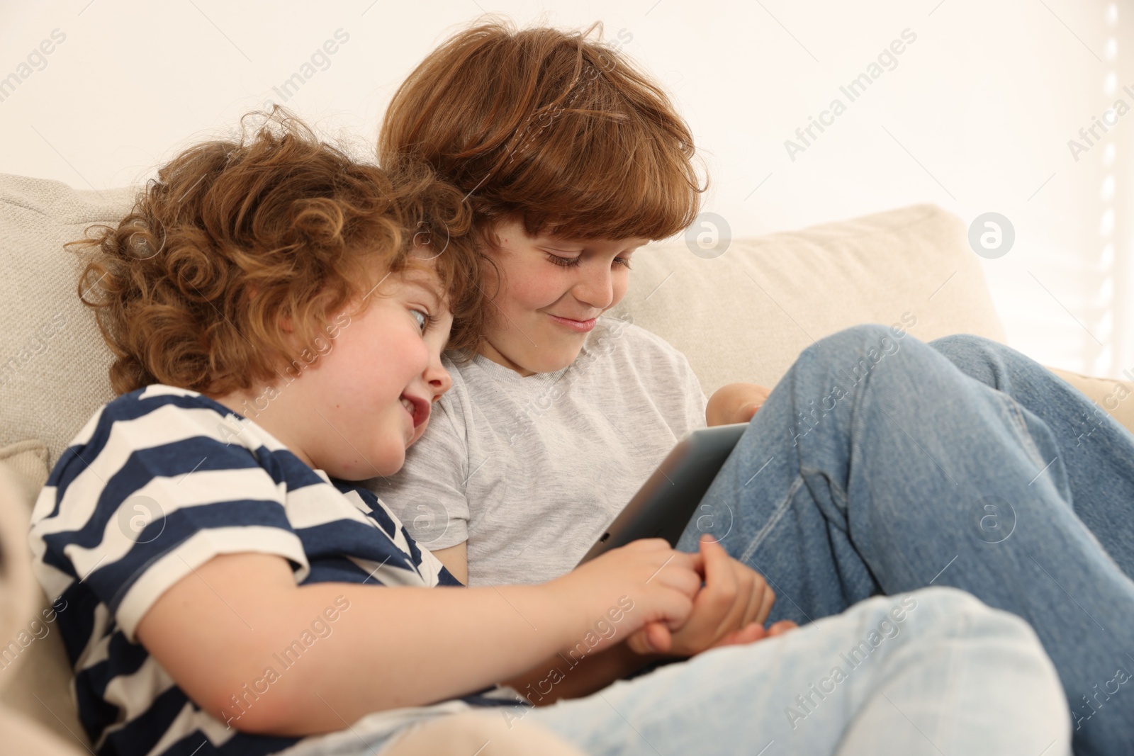 Cute little brothers with tablet on sofa at home Photo of Cute little brothers with tablet on sofa at home