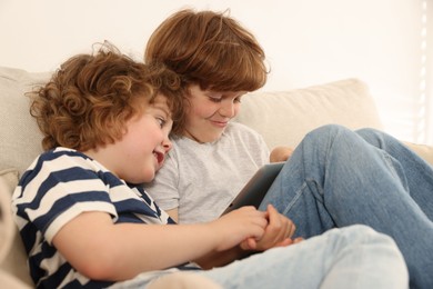 Photo of Cute little brothers with tablet on sofa at home