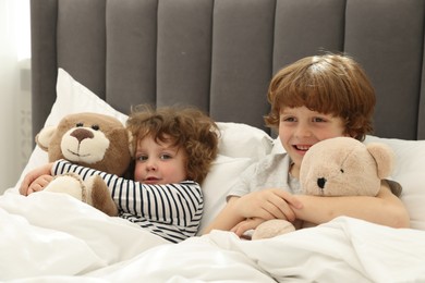 Photo of Cute little brothers with toys laying in bed at home