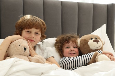 Photo of Cute little brothers with toys laying in bed at home