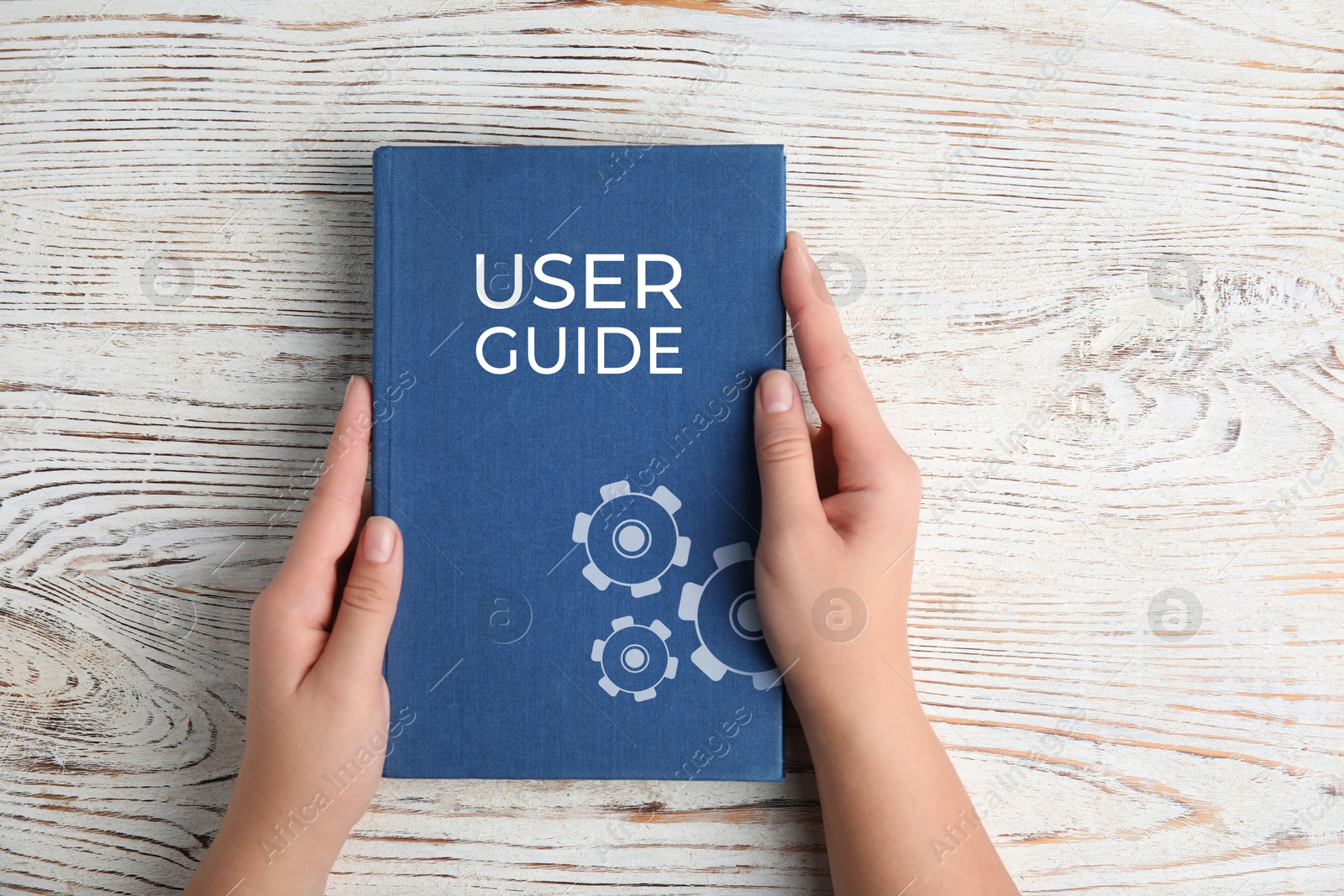 Woman holding User Guide book at white wooden table, top view Image of Woman holding User Guide book at white wooden table, top view