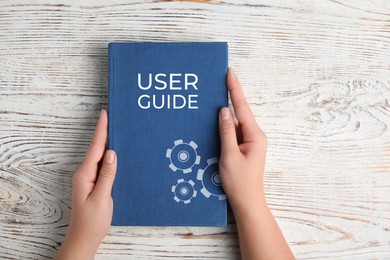 Image of Woman holding User Guide book at white wooden table, top view