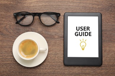 Image of User Guide document open in e-book device, cup of coffee and eyeglasses on wooden table, flat lay