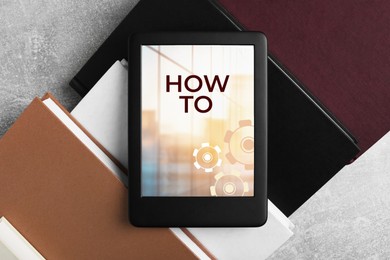 Image of How To document open in e-book device and different books on grey table, top view. User guide
