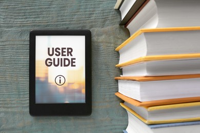 Image of User Guide document open in e-book device and different book on wooden table, top view