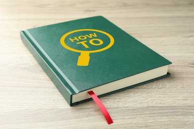 Image of How To book on wooden table, closeup. User guide