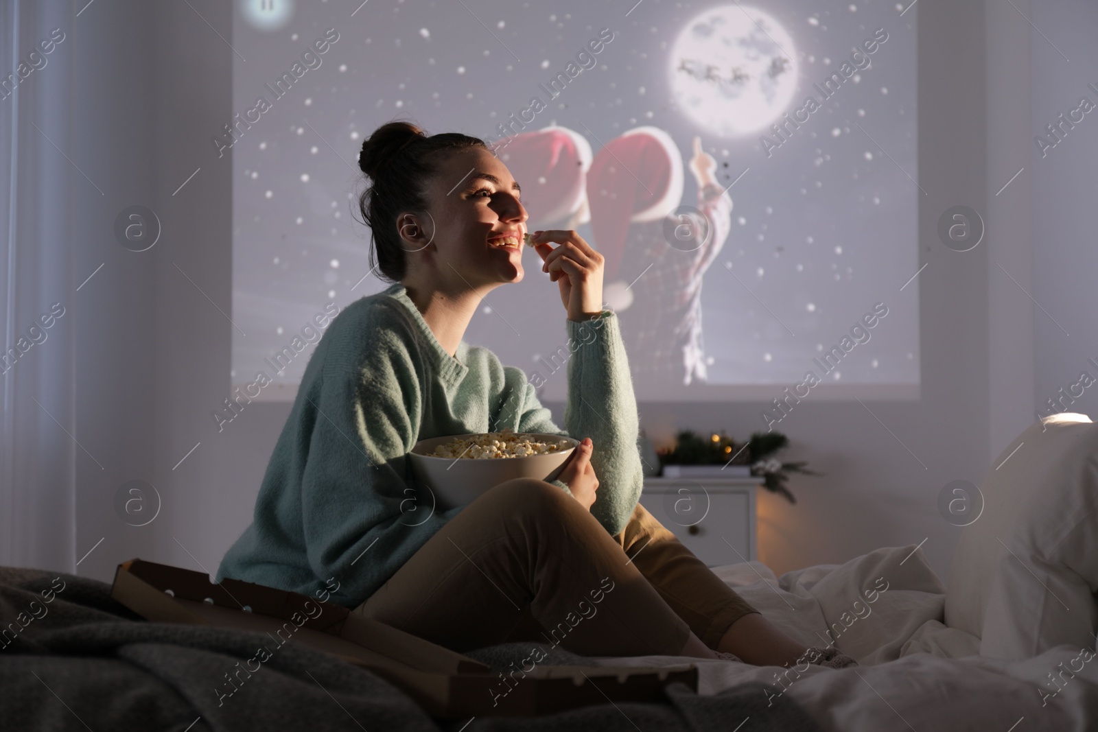 Woman with popcorn watching Christmas movie via video projector at home Photo of Woman with popcorn watching Christmas movie via video projector at home