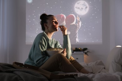 Photo of Woman with popcorn watching Christmas movie via video projector at home