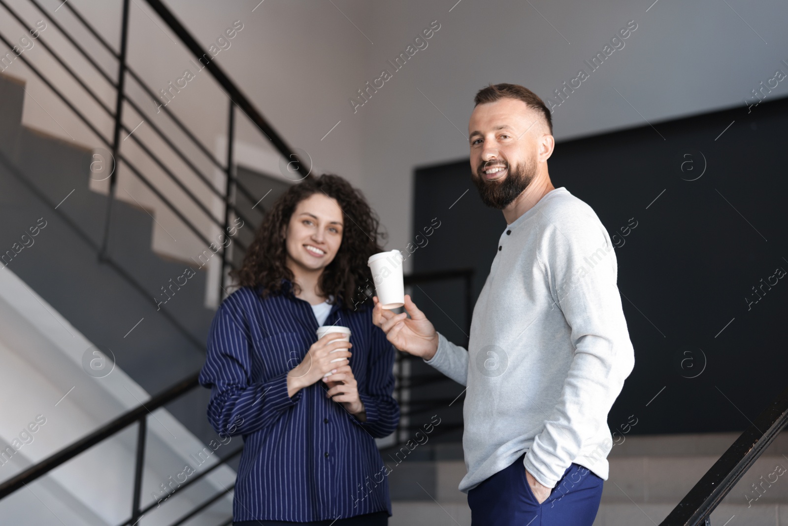 Colleagues with coffee on stairs in office during break Photo of Colleagues with coffee on stairs in office during break