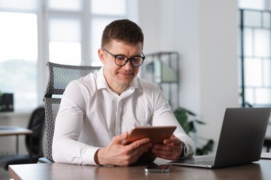 Photo of Man with tablet and laptop working at desk in office