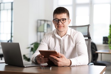 Photo of Man with tablet and laptop working at desk in office