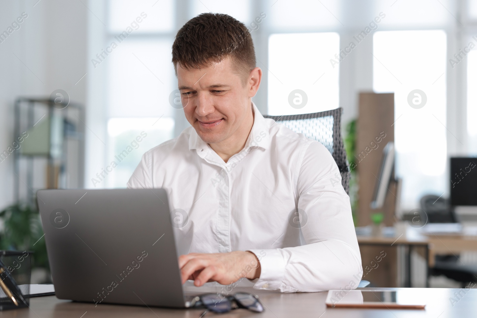 Man working on laptop at desk in office Photo of Man working on laptop at desk in office