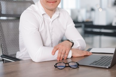 Photo of Man with laptop and glasses at wooden desk in office, closeup