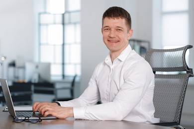 Photo of Man working on laptop at desk in office. Space for text