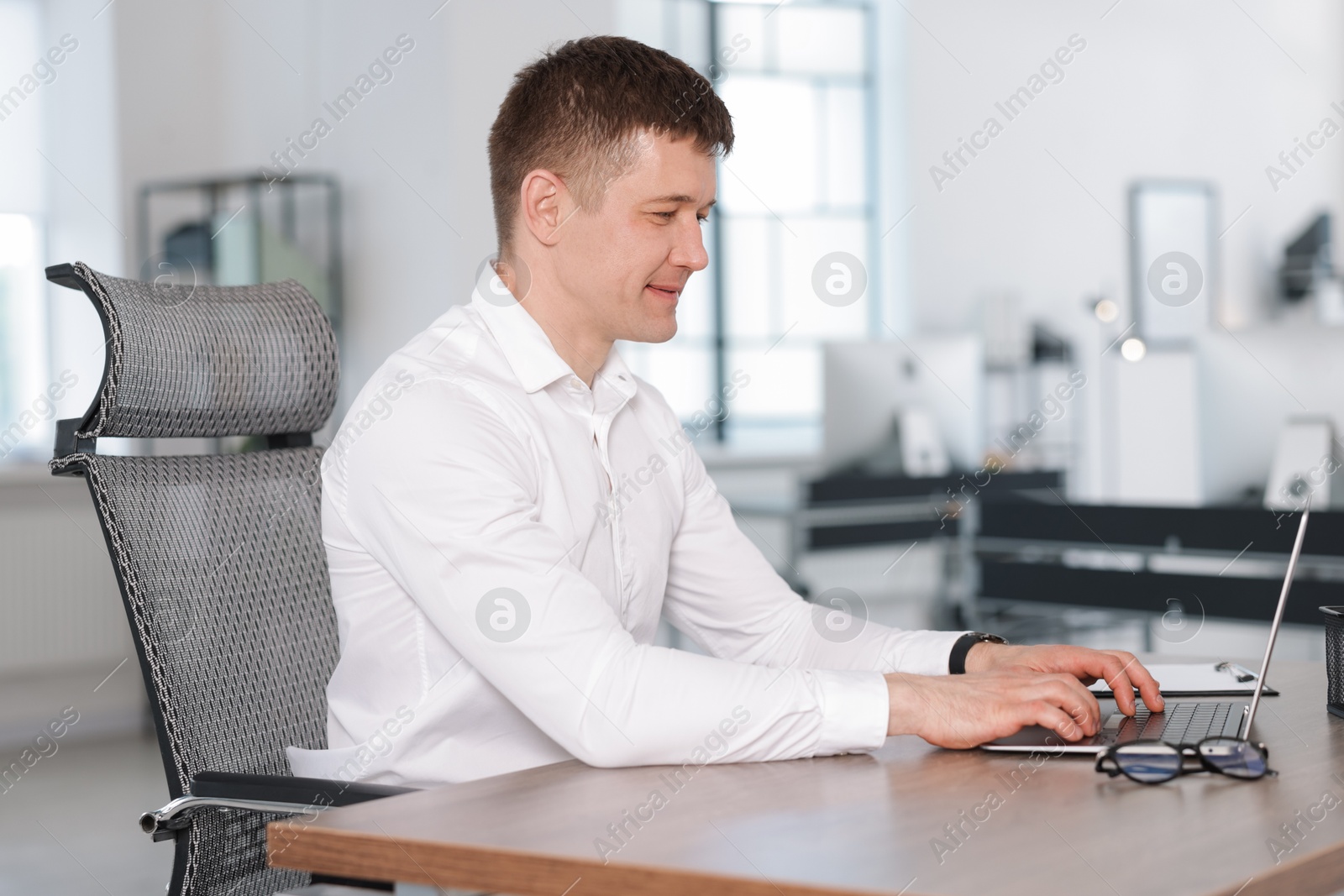 Man working on laptop at desk in office Photo of Man working on laptop at desk in office