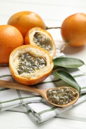 Photo of Ripe passion fruits, green leaves and seeds on white wooden table, closeup