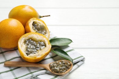 Photo of Ripe passion fruits, green leaves and seeds on white wooden table, closeup. Space for text