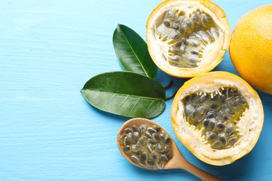 Photo of Ripe passion fruits, green leaves and seeds on light blue wooden table, above view. Space for text