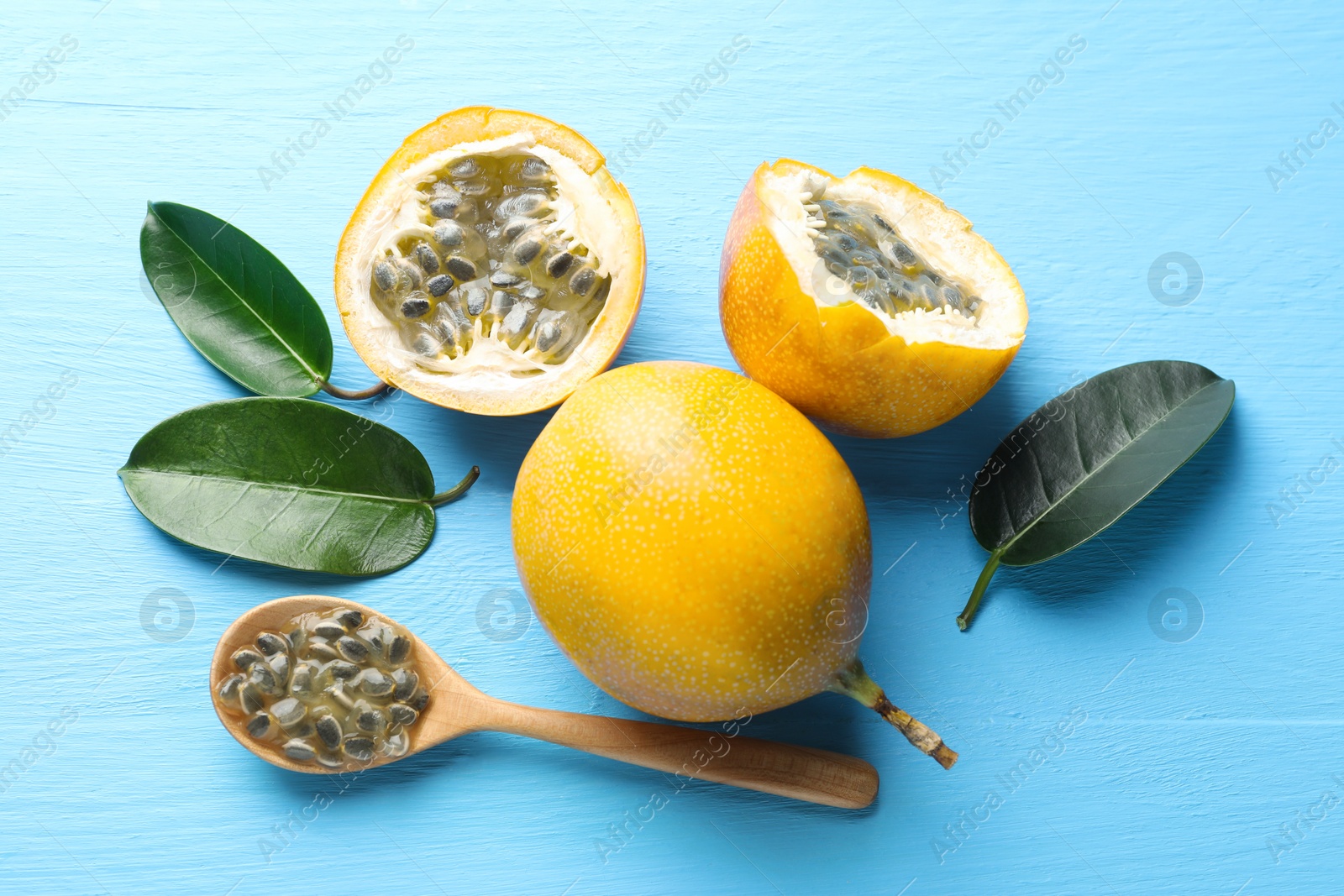 Ripe passion fruits, green leaves and seeds on light blue wooden table, flat lay Photo of Ripe passion fruits, green leaves and seeds on light blue wooden table, flat lay