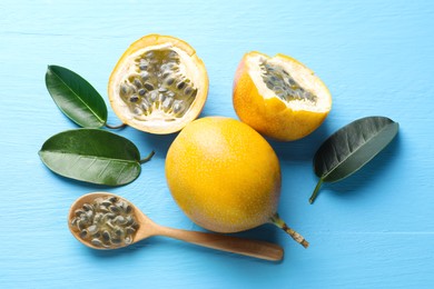 Photo of Ripe passion fruits, green leaves and seeds on light blue wooden table, flat lay