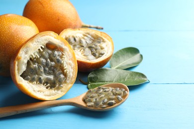 Photo of Ripe passion fruits, green leaves and seeds on light blue wooden table, closeup. Space for text
