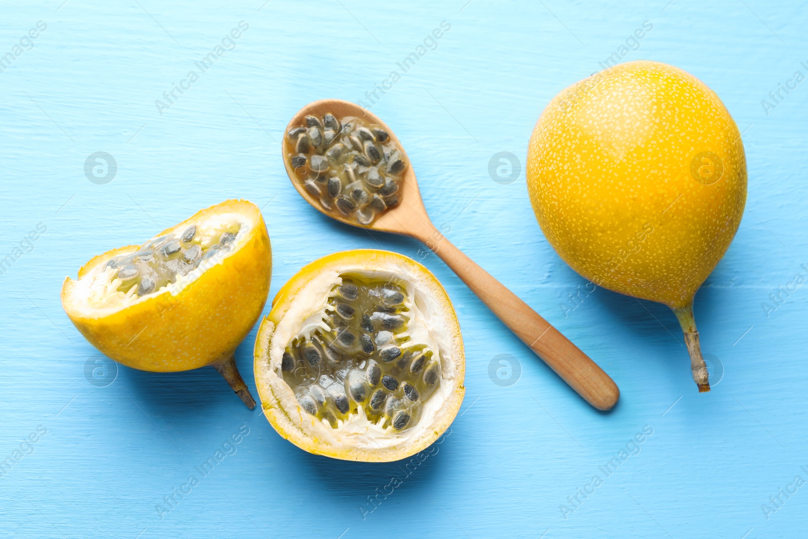 Photo of Ripe passion fruits and seeds on light blue wooden table, flat lay
