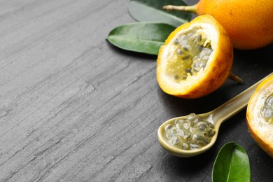 Photo of Ripe passion fruits, seeds and green leaves on black table, closeup. Space for text