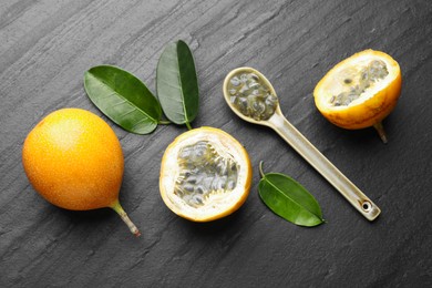 Photo of Ripe passion fruits, seeds and green leaves on black table, flat lay