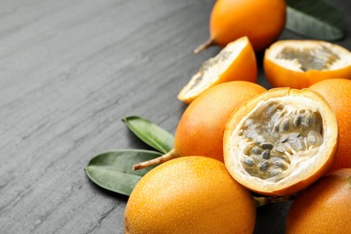 Photo of Ripe passion fruits and green leaves on black table, closeup. Space for text