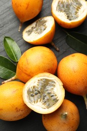 Photo of Ripe passion fruits and green leaves on black table, flat lay