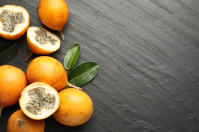 Photo of Ripe passion fruits and leaves on black table, flat lay. Space for text