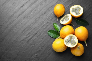 Photo of Ripe passion fruits and green leaves on black table, flat lay. Space for text