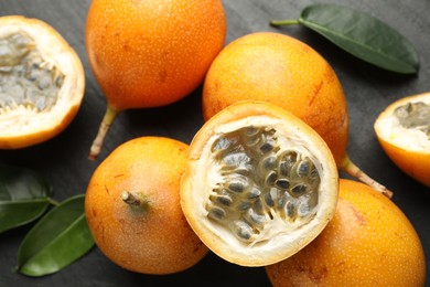 Photo of Ripe passion fruits and green leaves on black table, flat lay