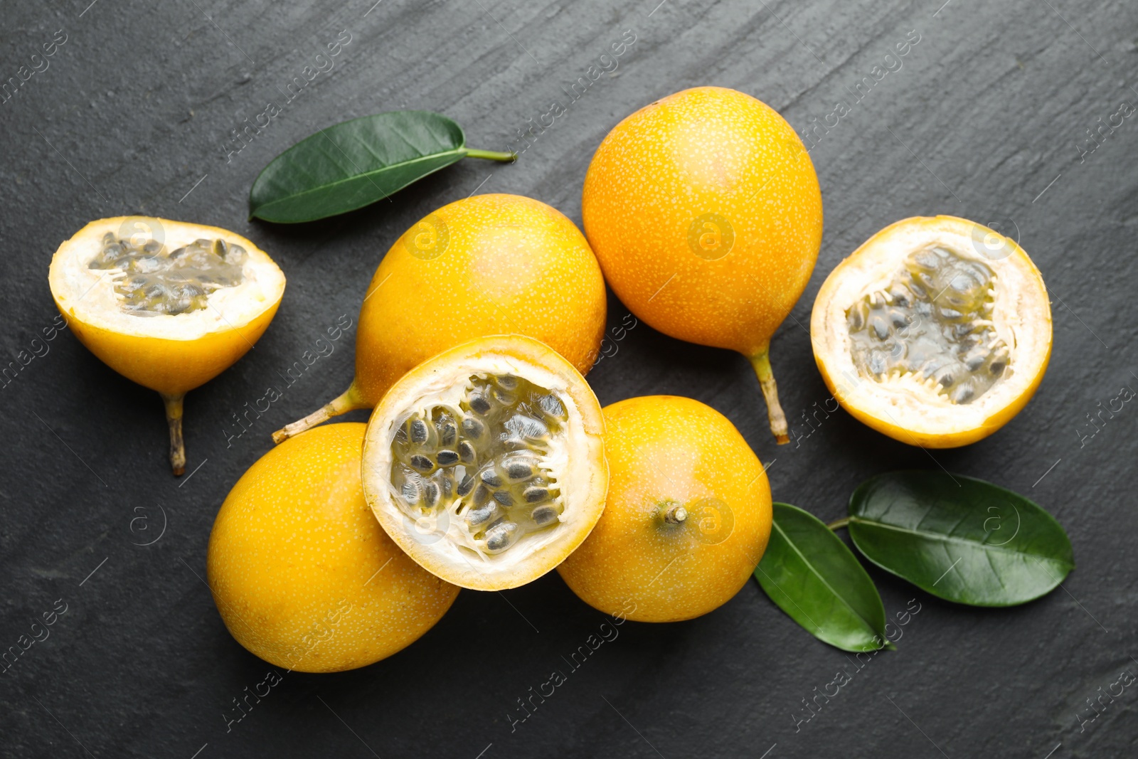 Ripe passion fruits and green leaves on black table, flat lay Photo of Ripe passion fruits and green leaves on black table, flat lay