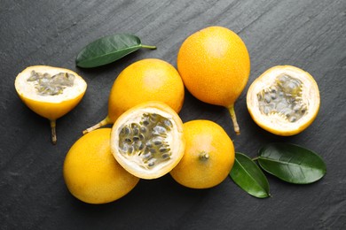 Photo of Ripe passion fruits and green leaves on black table, flat lay