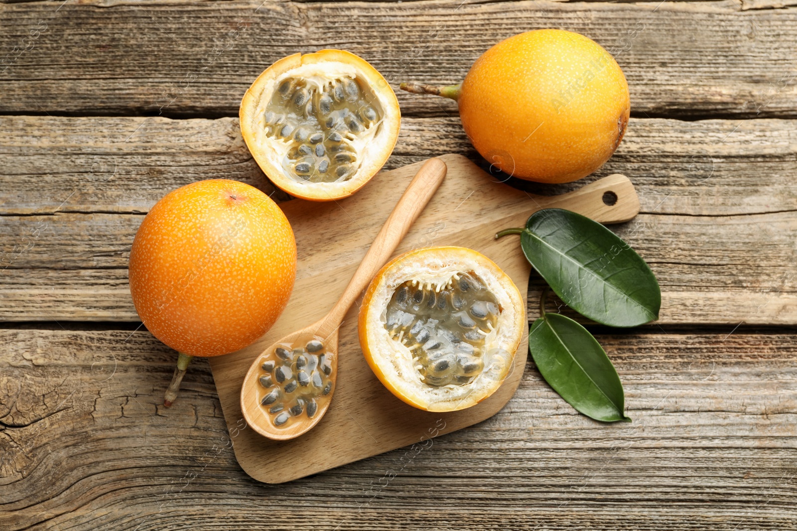 Photo of Ripe passion fruits, seeds and green leaves on wooden table, flat lay