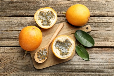 Photo of Ripe passion fruits, seeds and green leaves on wooden table, flat lay
