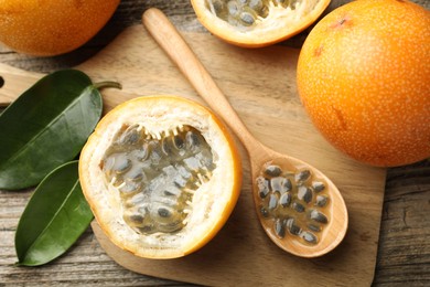 Photo of Ripe passion fruits, seeds and green leaves on wooden table, flat lay