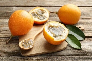 Photo of Ripe passion fruits, seeds and green leaves on wooden table, closeup