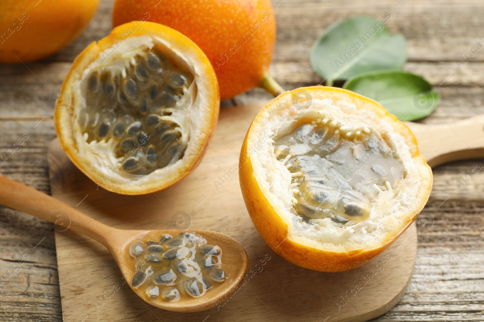 Photo of Ripe passion fruits, seeds and green leaves on wooden table, closeup