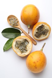 Photo of Ripe passion fruits, seeds and green leaves on white background, flat lay