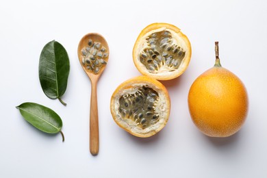 Photo of Ripe passion fruits, seeds and green leaves on white background, flat lay