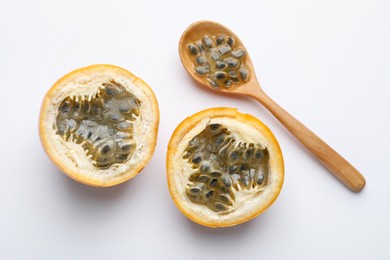 Photo of Halves of ripe passion fruit, seeds and spoon on white background, flat lay
