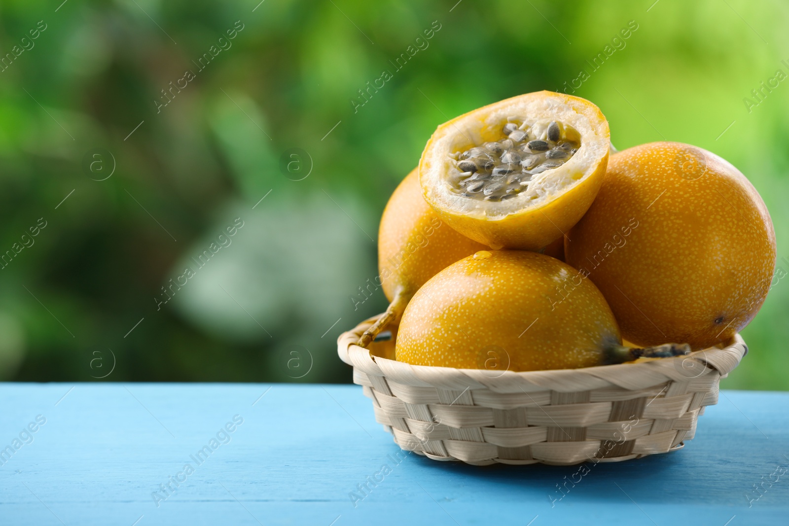 Ripe passion fruits in wicker basket on light blue wooden table outdoors, closeup. Space for text Photo of Ripe passion fruits in wicker basket on light blue wooden table outdoors, closeup. Space for text