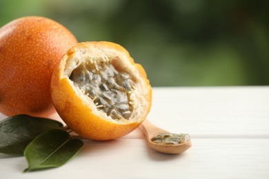 Photo of Ripe passion fruits, green leaves and seeds on white wooden table outdoors, closeup. Space for text